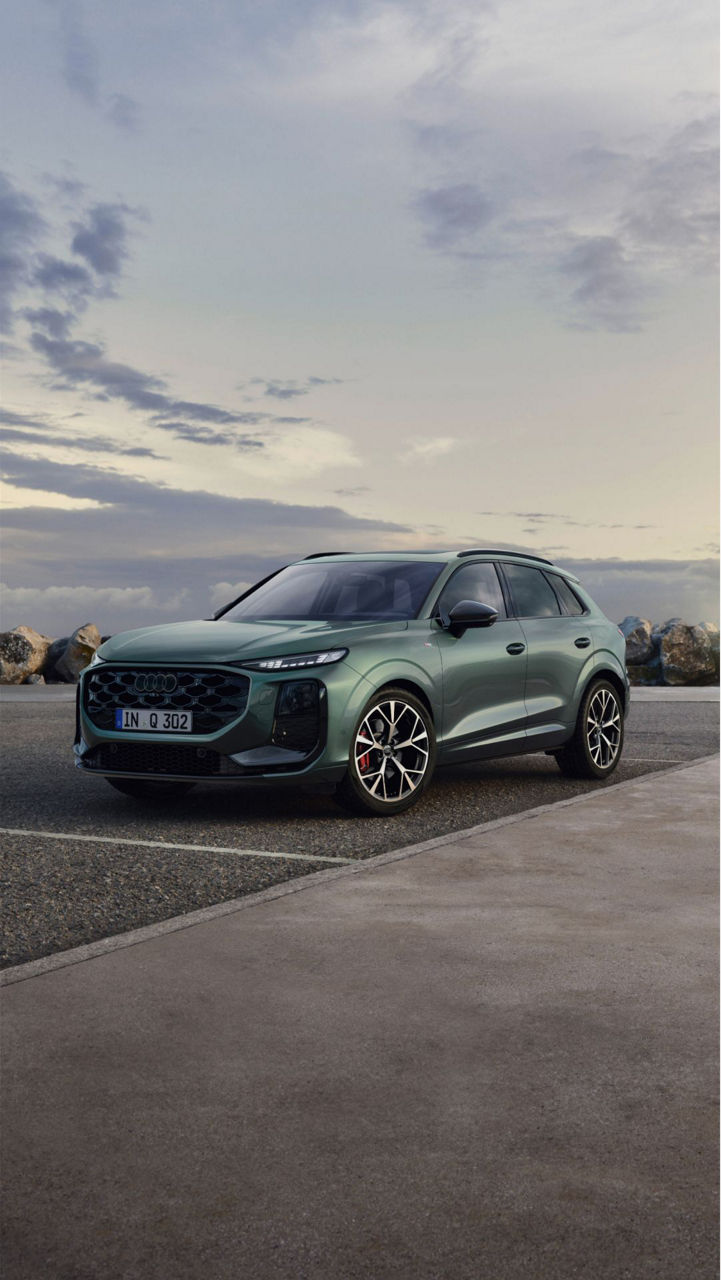 Audi Q3 parked on a coastal road with rocky shores in the background under a cloudy sky, showcasing modern design.