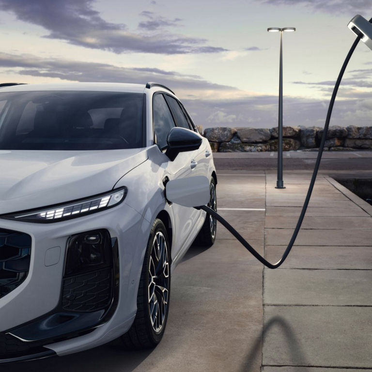 Front view of a white Audi Q3 e-hybrid plugged in an EV charger