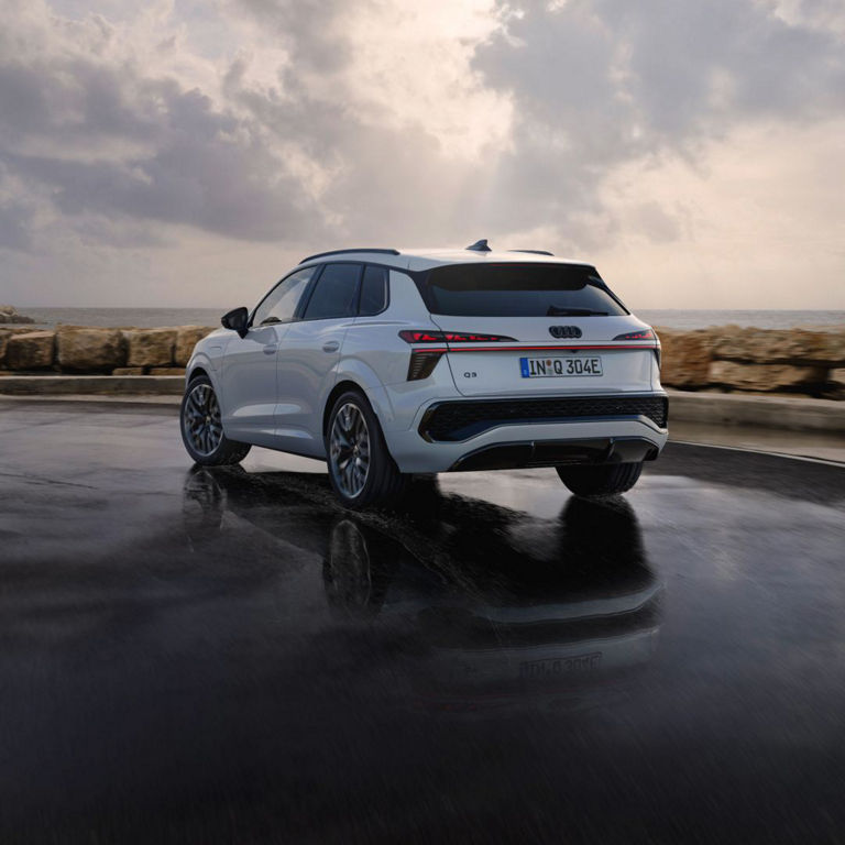 Rear shot of a white Audi parked near the sea with a rocky wall at the background