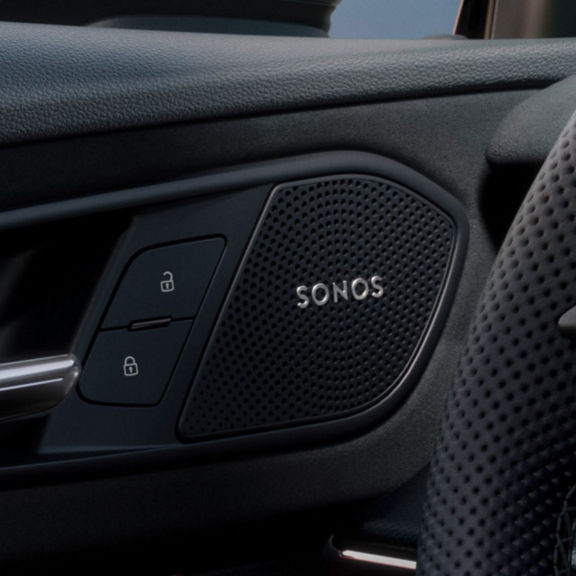Close-up of Audi Q3 interior door showing Sonos speaker, door handle, lock buttons, and steering wheel detail.