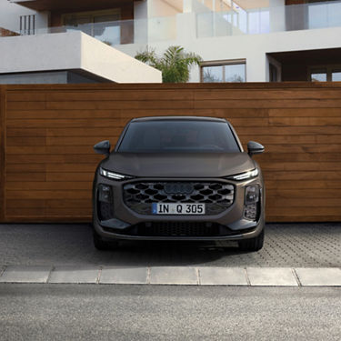 Front view of a matte black Audi Q3 parked in front of a modern house with a wooden garage door.