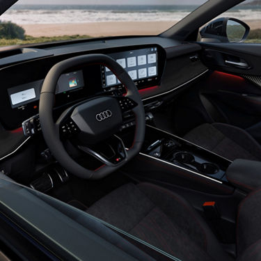 Audi Q3 cockpit with digital displays, sporty steering wheel, red-stitched seats, and beach view outside.