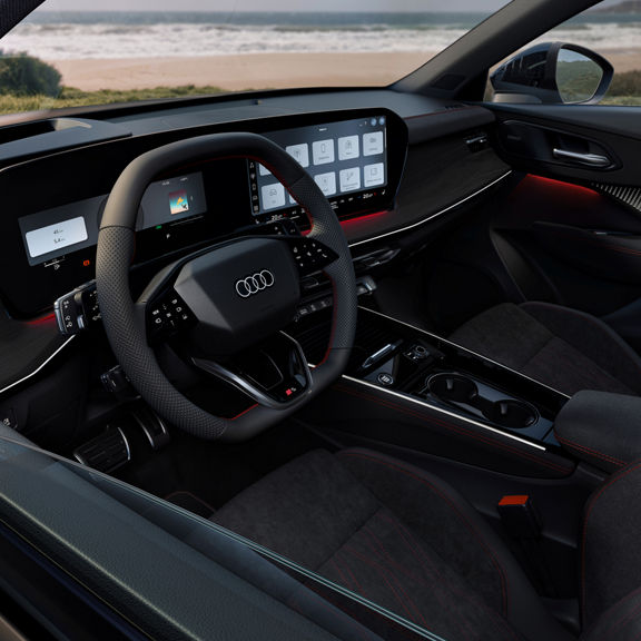 Audi Q3 interior with digital cockpit, touchscreen controls, and red-stitched seats, overlooking a beach.
