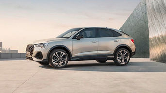 Silver Audi Q3 Sportback parked on a rooftop with city skyline and modern geometric building in background.