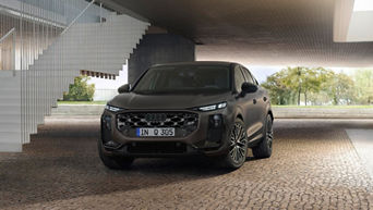 A green Audi Q5 Sportback driving on a winding road against a backdrop of mountains at sunset.