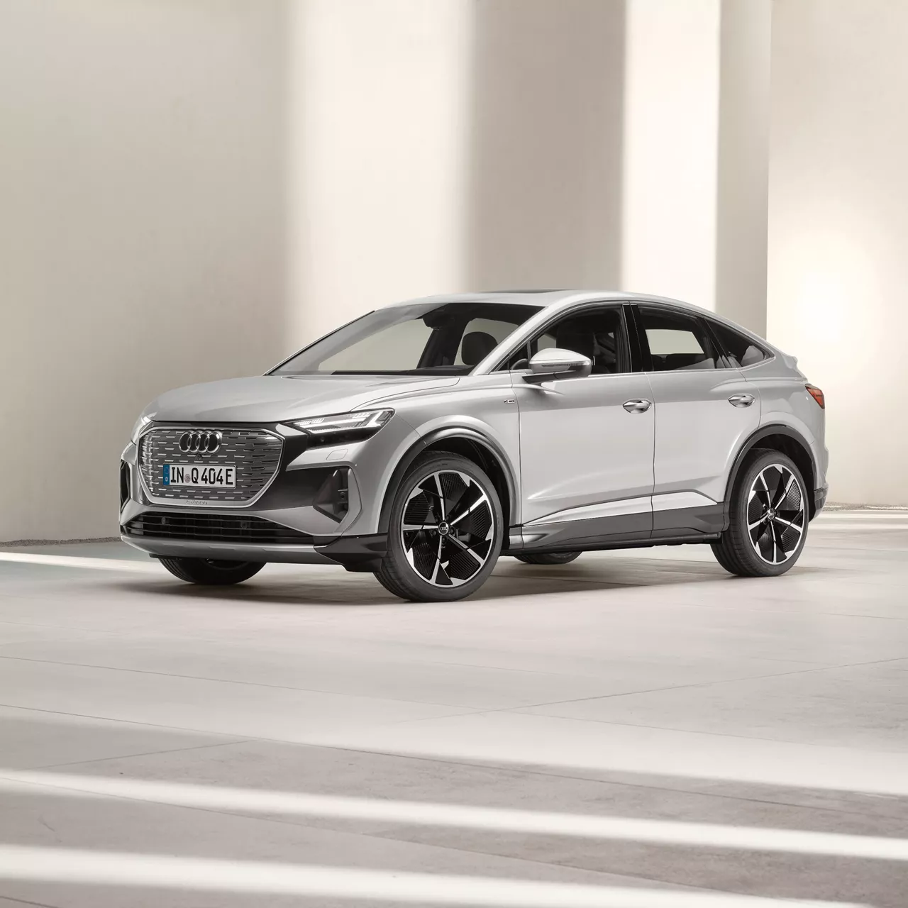 A silver Audi Q4 Sportback e-tron parked on a modern, minimalist background with soft lighting and geometric shadows.
