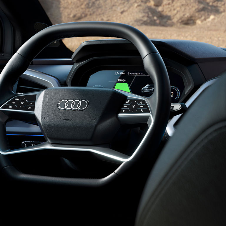 Close-up of the modern steering wheel and dashboard in an Audi Q4 Sportback e-tron, featuring a digital display with navigation and range information.