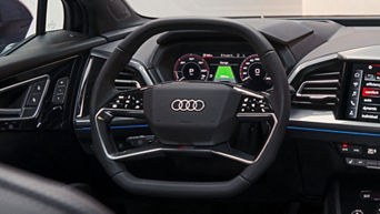 Close-up of an Audi steering wheel with controls, digital displays showing speed and range.