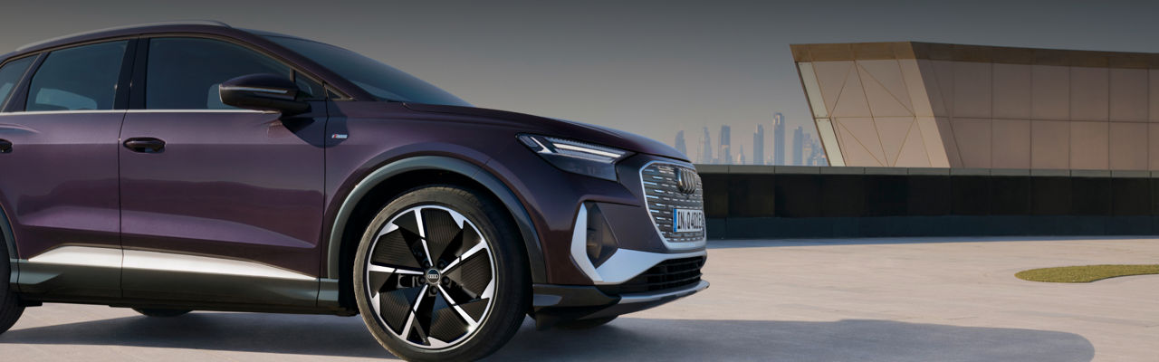 A purple electric SUV parked with a modern building and city skyline in the background.