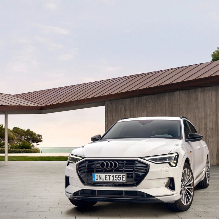 White Audi car parked by a modern house with a sea view in the background.