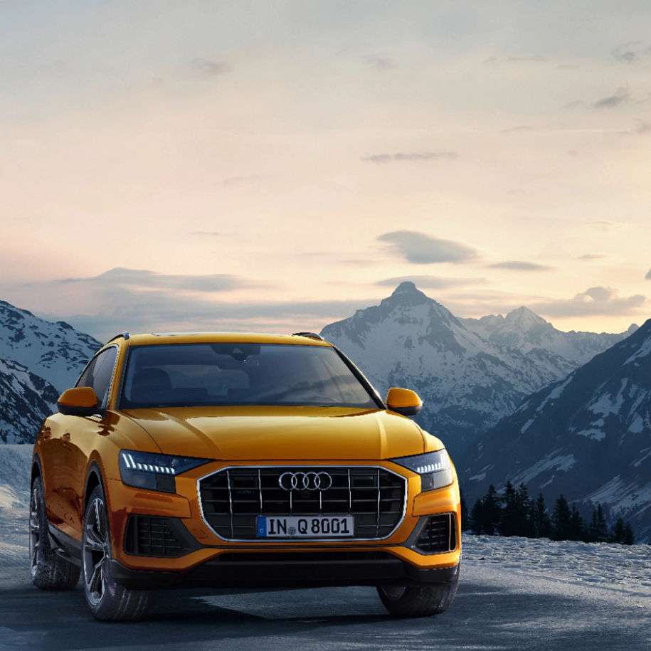 A yellow Audi SUV parked with a backdrop of snowy mountains at dusk.