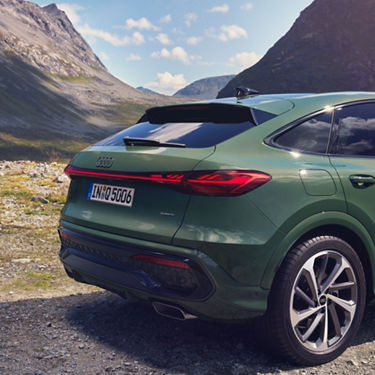 Rear close-up of a green Audi SUV, parked outdoors with a tall mountain in the background.