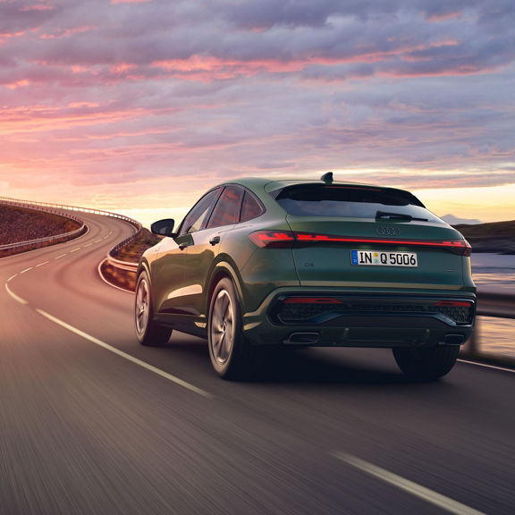 A dark green Audi SUV driving on a lake view road, from a rear view perspective.