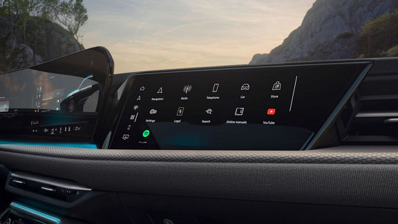 Close-up of a modern car dashboard with a digital display featuring navigation, media, and app icons against a scenic background.