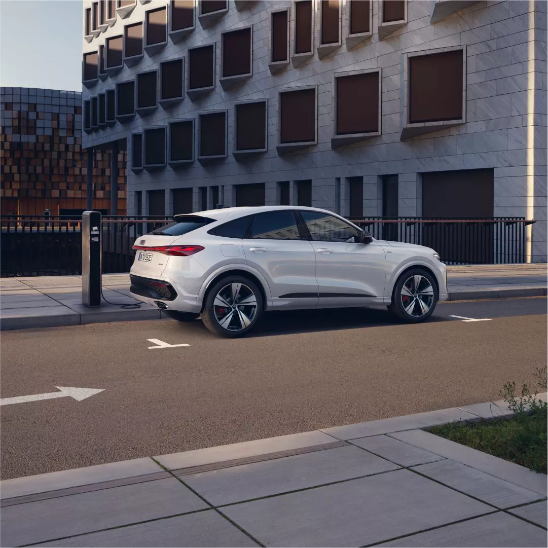 A white Audi SUV parked at a charging station amidst modern urban architecture.