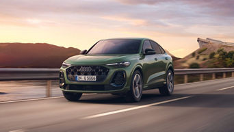 A green Audi Q5 Sportback driving on a winding road against a backdrop of mountains at sunset.