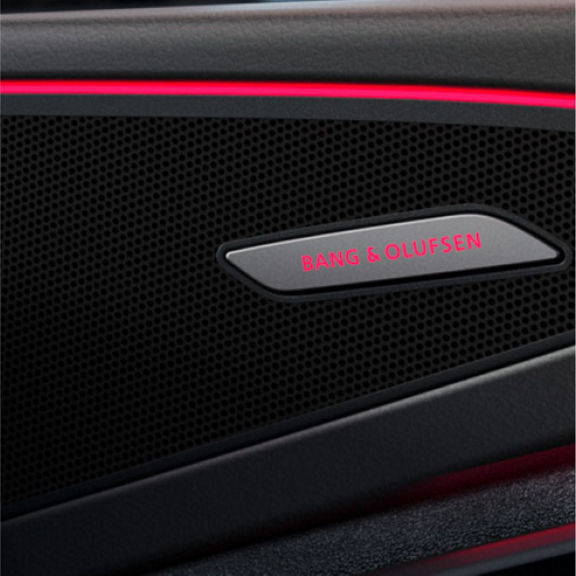 Close-up of a car speaker grille featuring a Bang & Olufsen logo illuminated by a subtle red light.