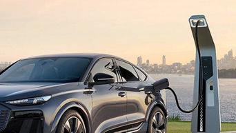 Silver Audi car plugged in an EV charger with water and city in the background