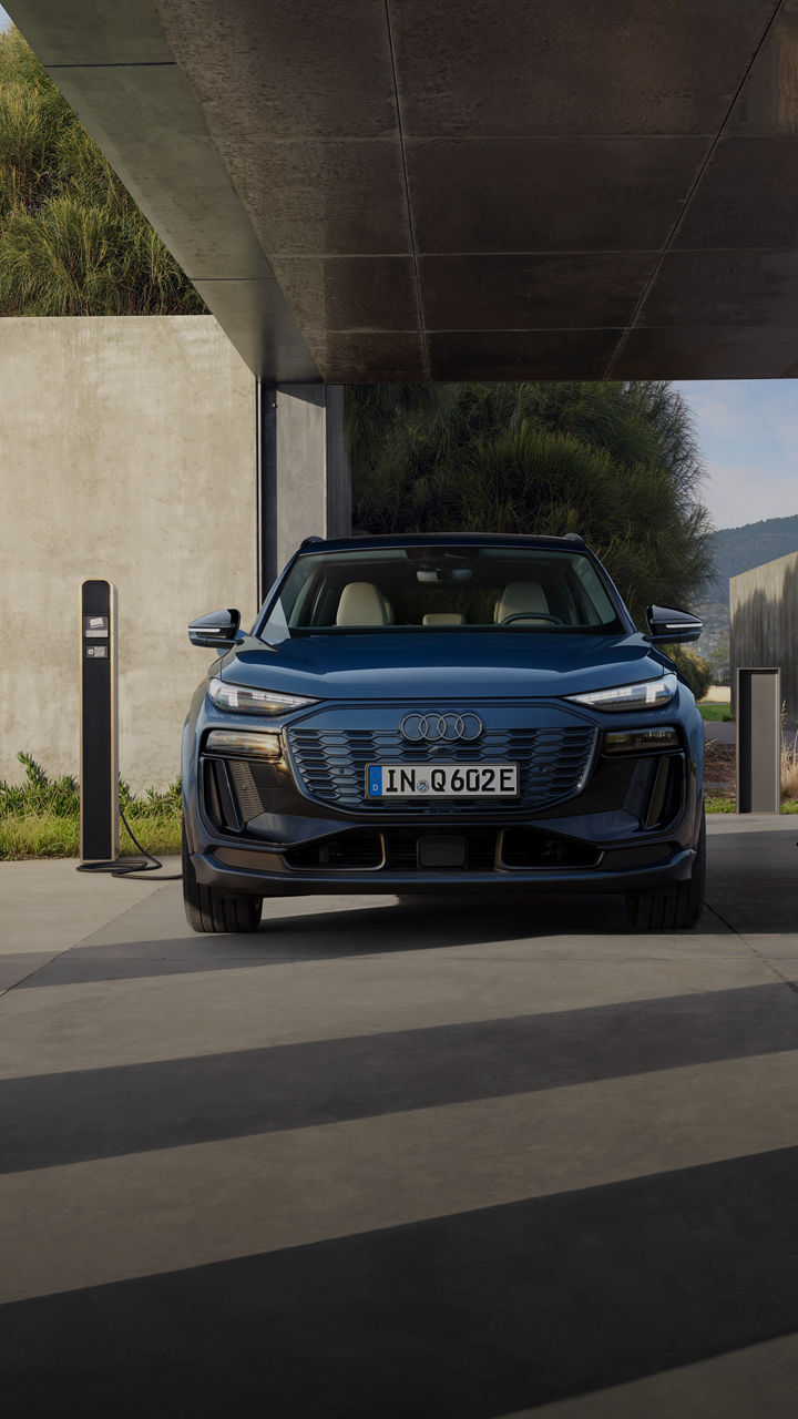 A woman walks past a parked blue Audi Q6 SUV e-tron with a charger, focused on her phone.