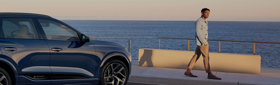 A blue SUV parked by the seaside at dusk, with a person walking in the background.
