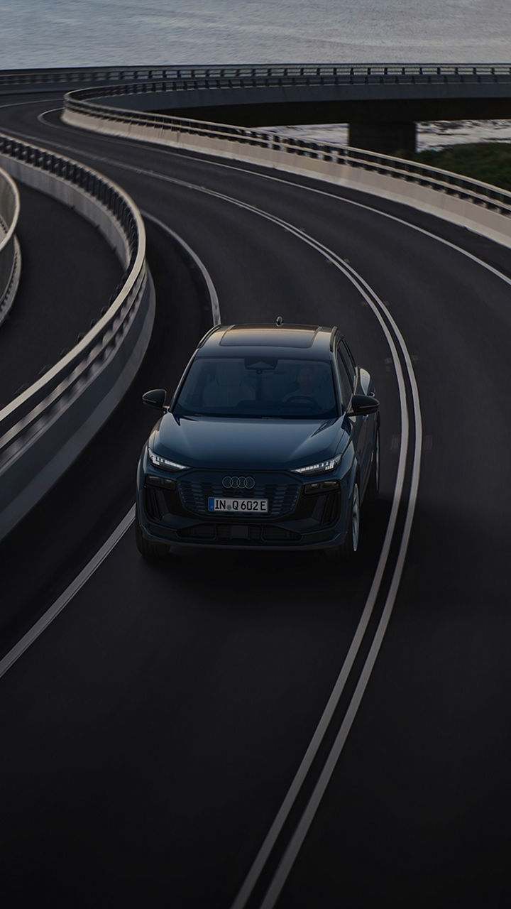 An Audi car driving on a curved coastal road with guardrails, ocean and cliffs in the background.