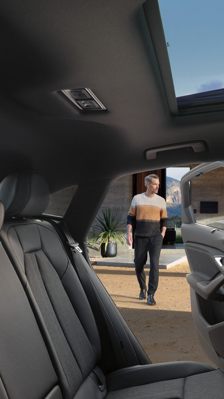 Interior view of a car showcasing sleek grey seats, a panoramic sunroof, and a person walking towards an outdoor setting.
