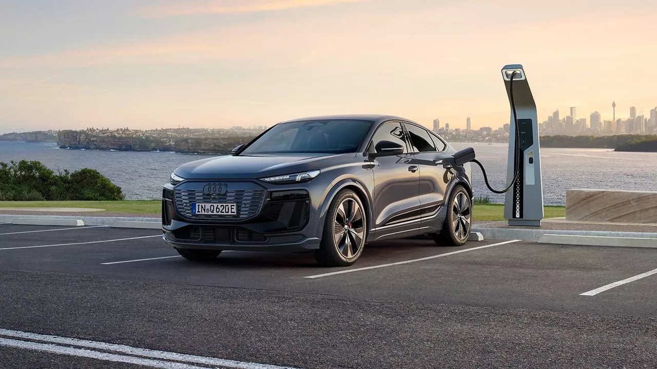 A sleek electric SUV charging at a modern station with a city skyline and sunset in the background.