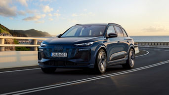 Blue Audi Q6 e-tron SUV driving on a curved road with sea at the far back