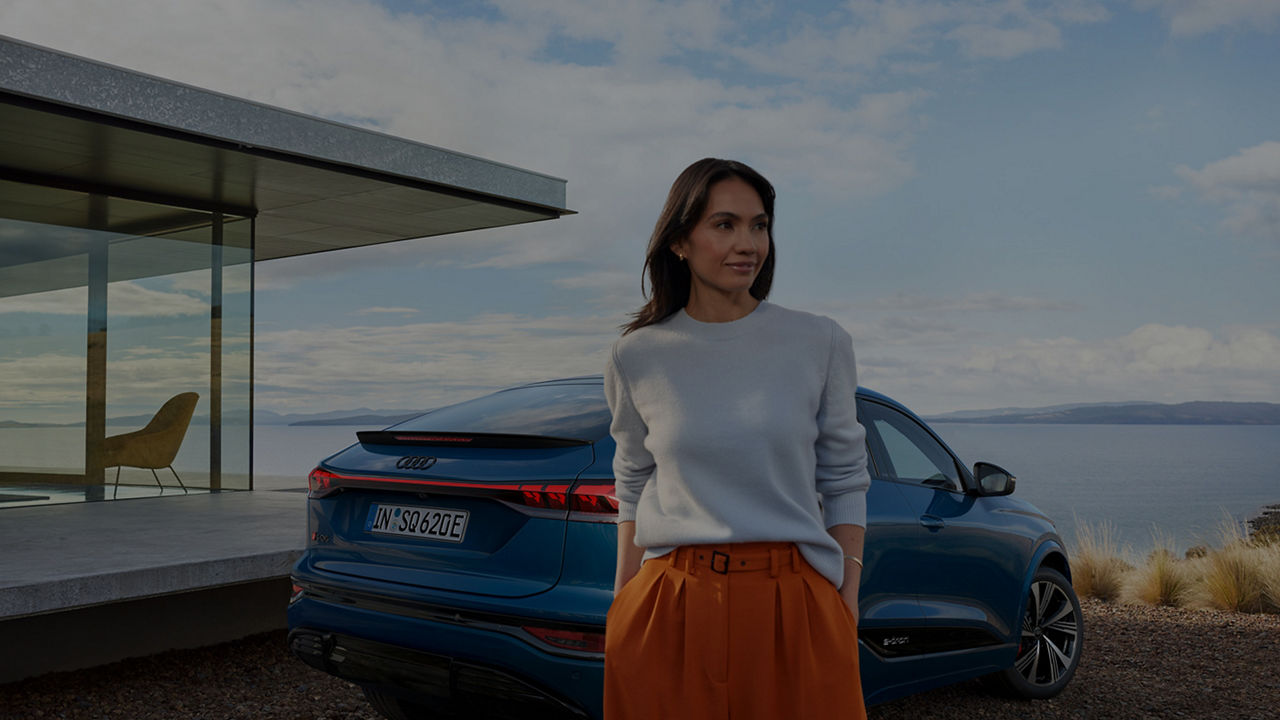 A woman dressed elegantly with her hands in her pockets standing in front of an Audi SQ6 Sportback e-tron