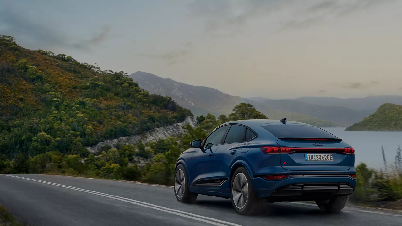 A blue Audi SQ6 Sportback e-tron driving down a scenic road with lake and mountains in the background