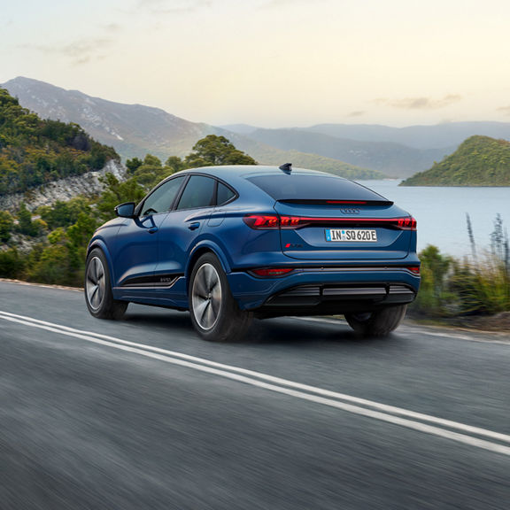 A blue Audi SQ6 Sportback e-tron driving on a scenic lakeside road