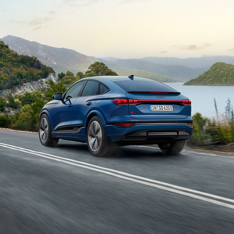 A blue Audi SQ6 Sportback e-tron driving on a scenic lakeside road