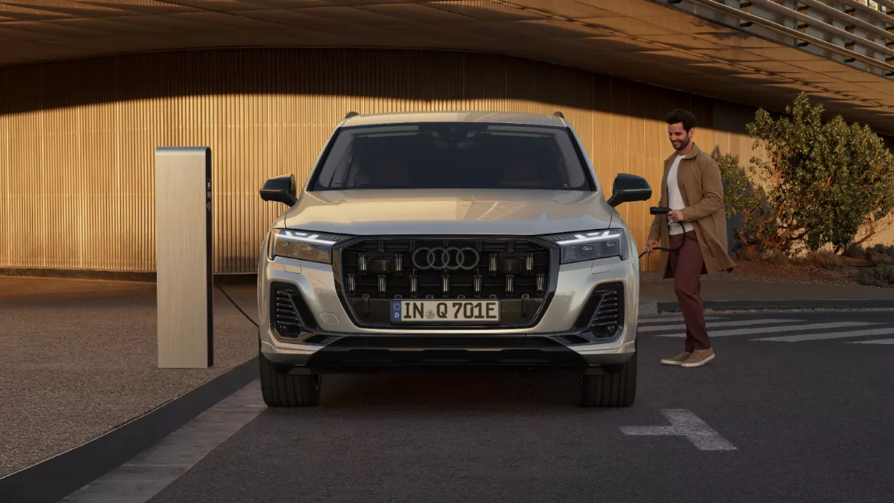 A white Audi Q7 TFSI e next to an EV charger and man standing on the right