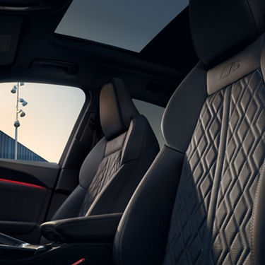 Car interior with dark quilted leather seats, with natural sunlight coming through.