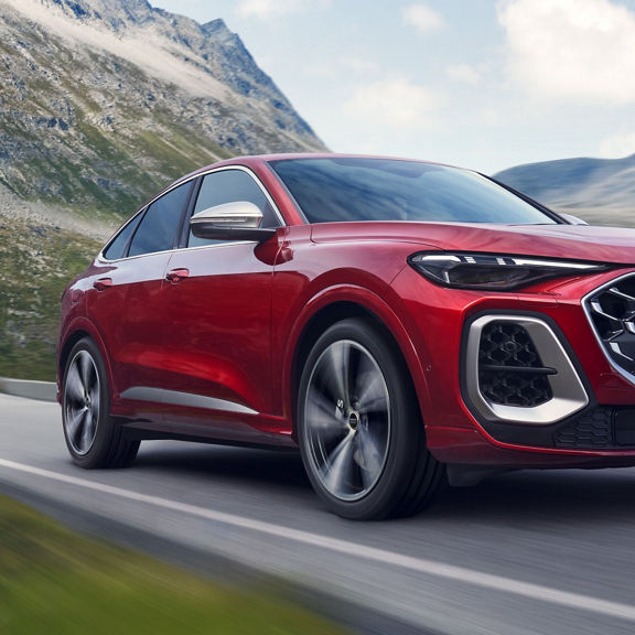 A red Audi SUV driving through a mountain road.