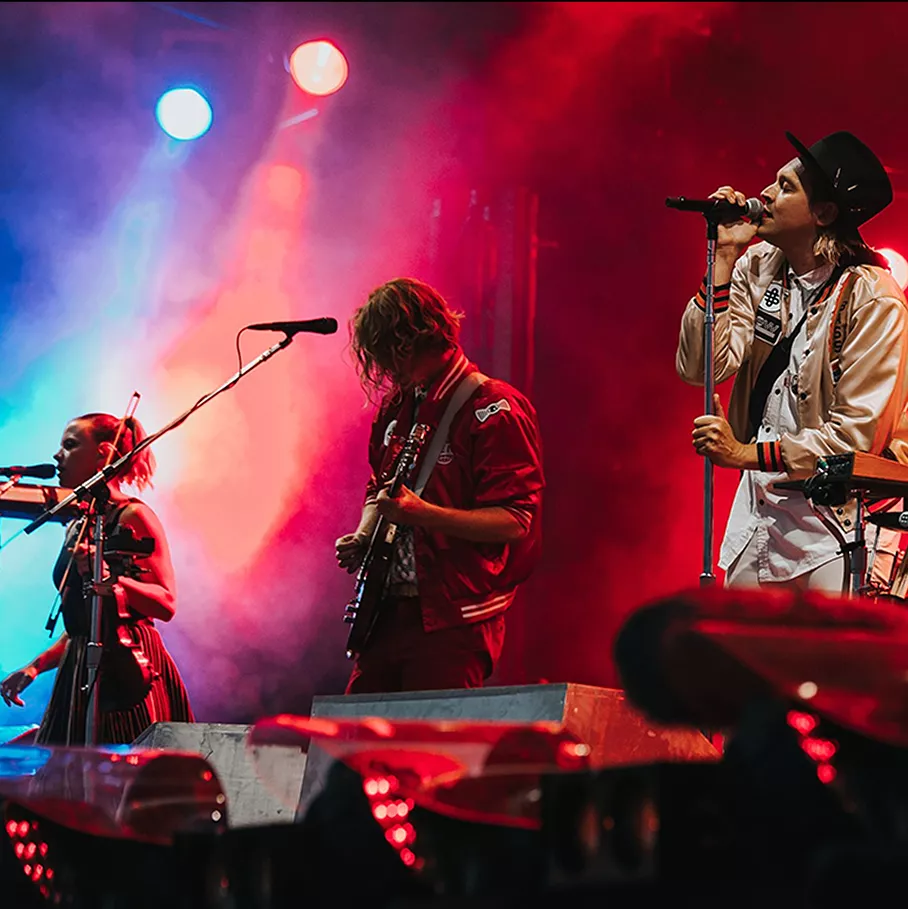 A vibrant live music performance featuring a band on stage illuminated by blue and red lights, with members playing instruments passionately.