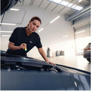 A mechanic in red overalls with Audi logo changing a car's oil