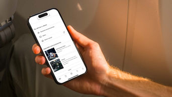 A person holding a smartphone displaying the myAudi app with vehicle details and customisation options