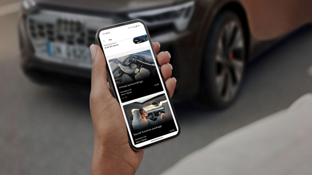 A person holds a smartphone displaying the Audi Functions Store, featuring parking assist options for an Audi vehicle.