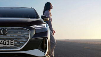 A woman standing against the passenger side of a parked Audi vehicle