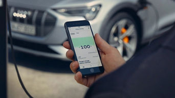 Person holding their phone which is displaying the myAudi app, Audi car parked in the background