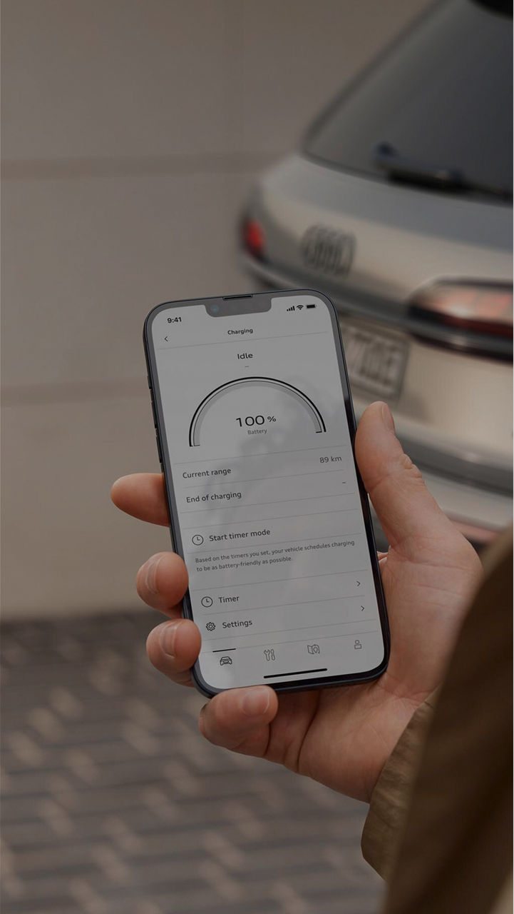 Person holding a phone interactive with the myAudi app, Audi vehicle in the background