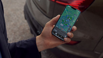 A hand holding a mobile phone with the myAudi app on screen displaying nearest charge stations