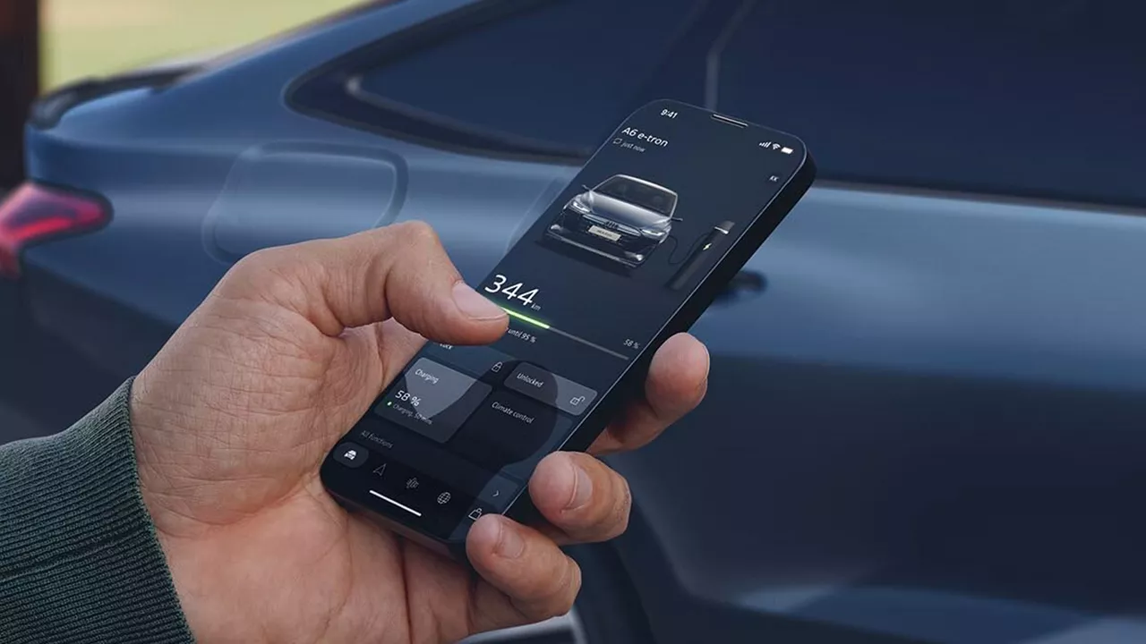 A person holding a smartphone displaying the myAudi app with an Audi vehicle blurred in the background.