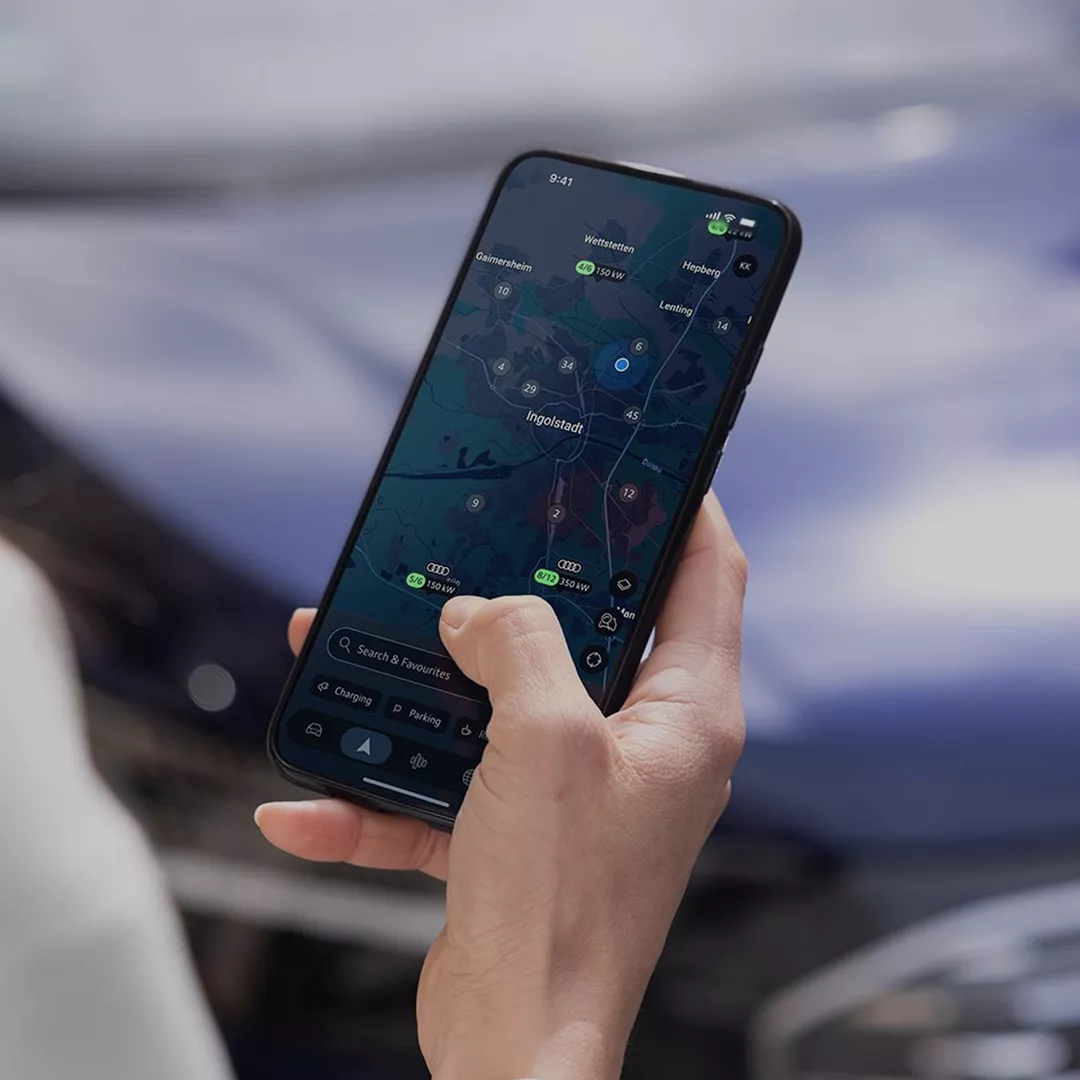 A person in a cream bomber jacket and gray pants stands outside, engaged with their smartphone.