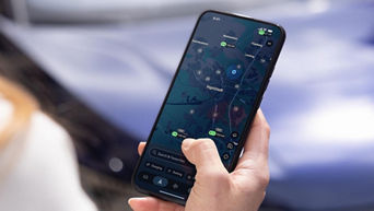 A close-up of a hand interacting with a smartphone displaying a charging station map next to an Audi vehicle.