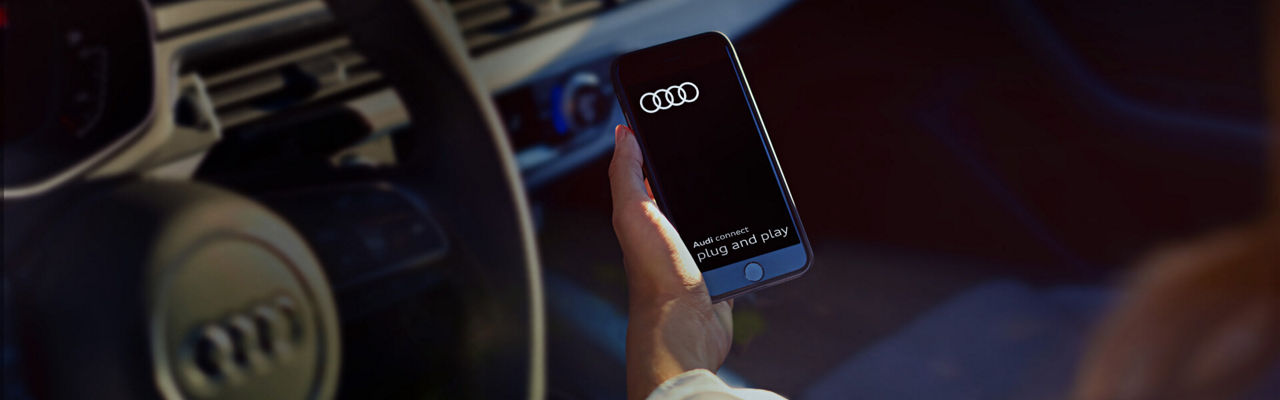 A hand holding a mobile phone displaying the Audi Connect Plug & Play app