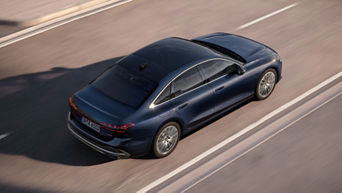 A sleek blue Audi sedan speeds along a smooth road, showcasing its elegant design and modern silhouette from an aerial view.