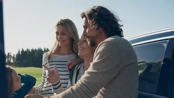 A family standing in front of a car car, smiling and chatting