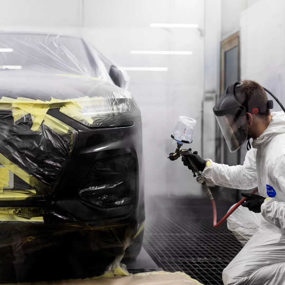 Black Audi covered getting a paint job by man wearing white suit and mask